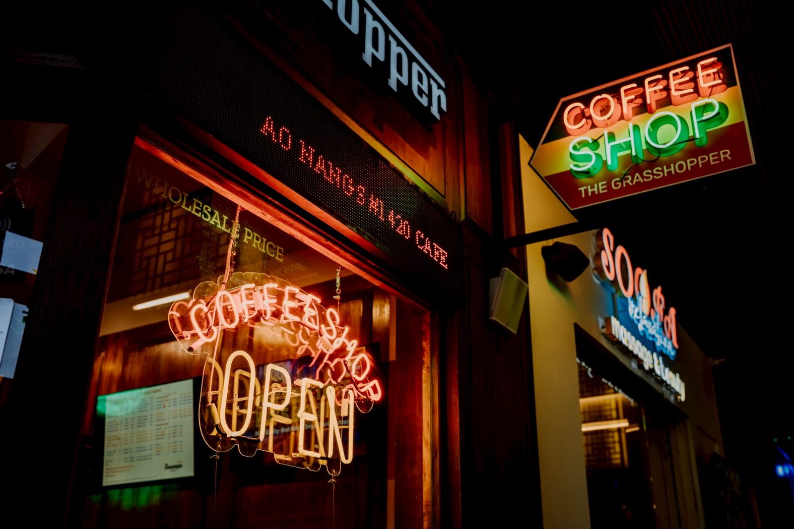 Neon “Coffee Shop Open” and “Coffee Shop” signs glowing in The Grasshopper’s windows at night