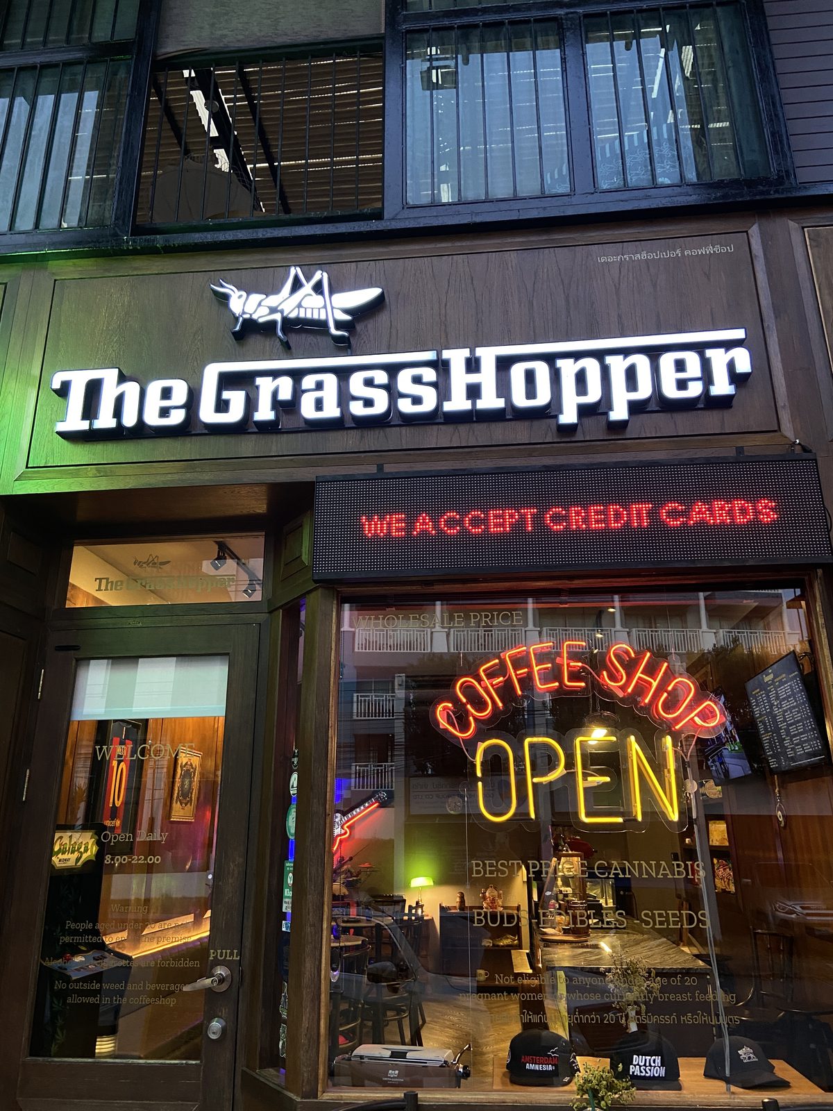 Front of COFFEESHOP THE GRASSHOPPER in Ao Nang: white The Grasshopper sign and a neon Coffee Shop Open sign in the window